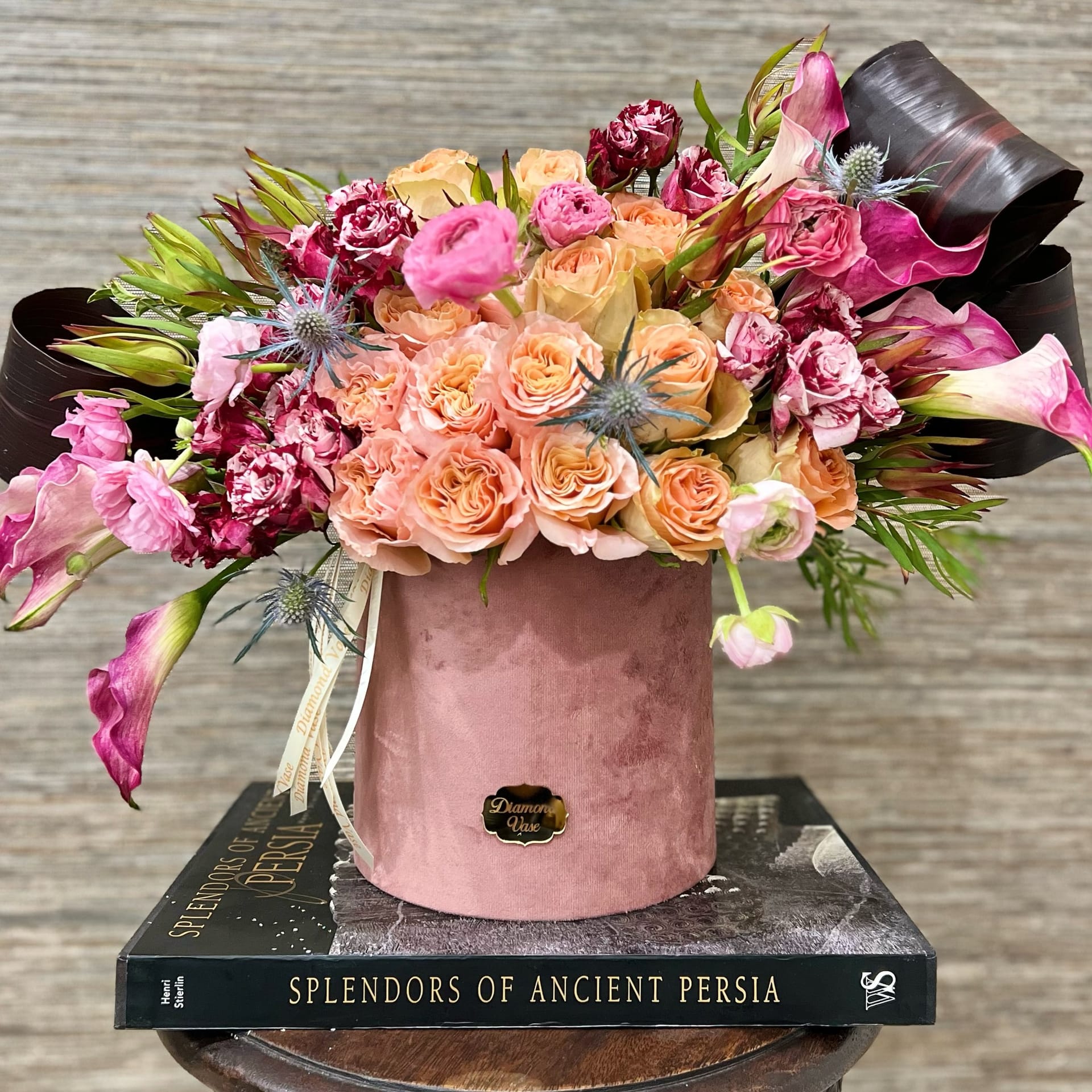 Peach garden roses, hot-pink ranunculus and magenta calla lilies in a dusty-rose velvet box