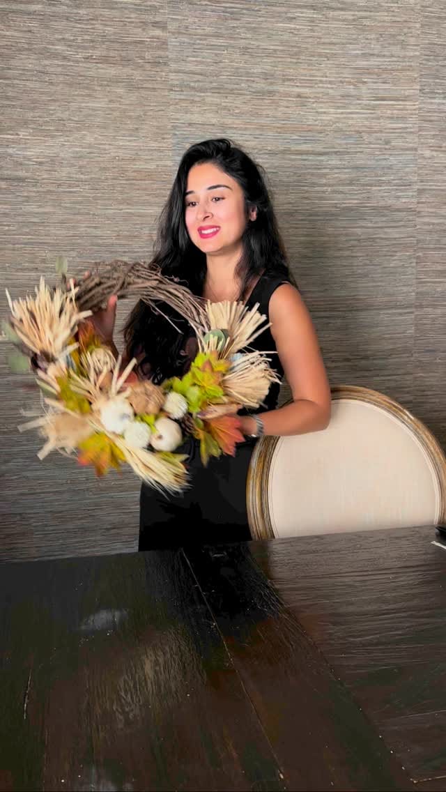 Bita smiling and holding a dried fall wreath of wheat, cotton and mini pumpkins