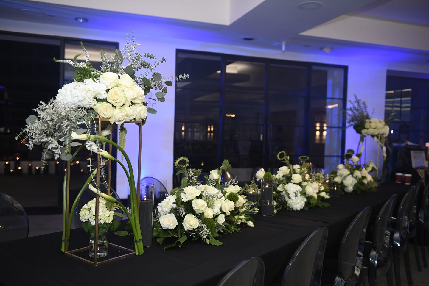 Bar Mitzvah head table in a blue-lit ballroom with a tall gold stand of white roses and candlelight