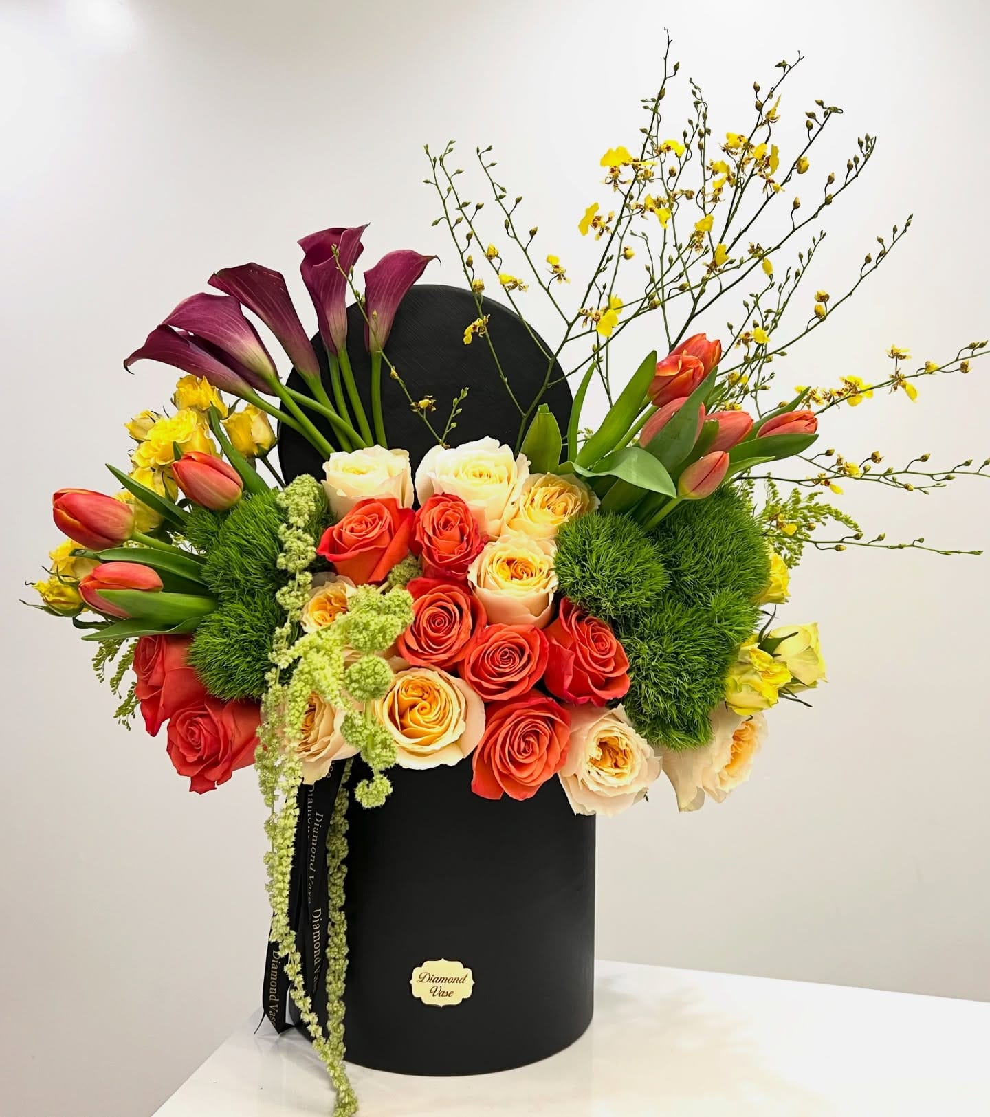 Coral roses, cream garden roses, orange tulips and burgundy calla lilies in a black Diamond Vase box