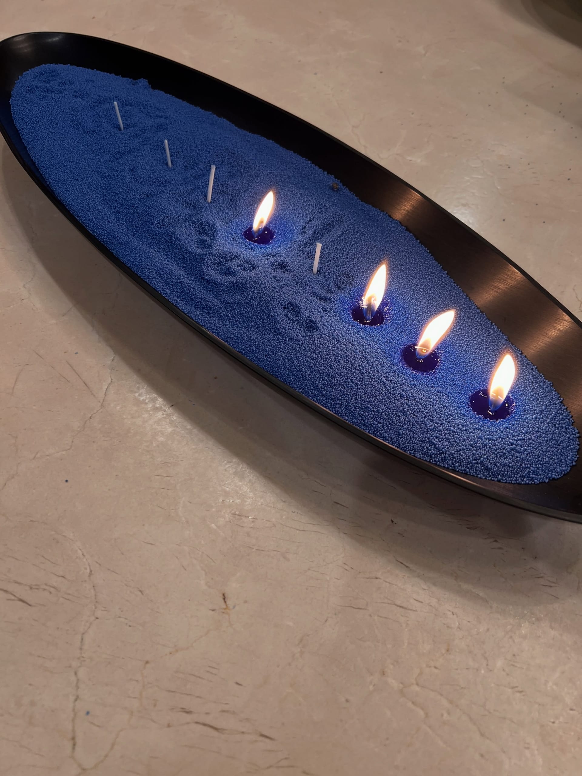Royal-blue candle sand with four lit wicks in a black oval tray