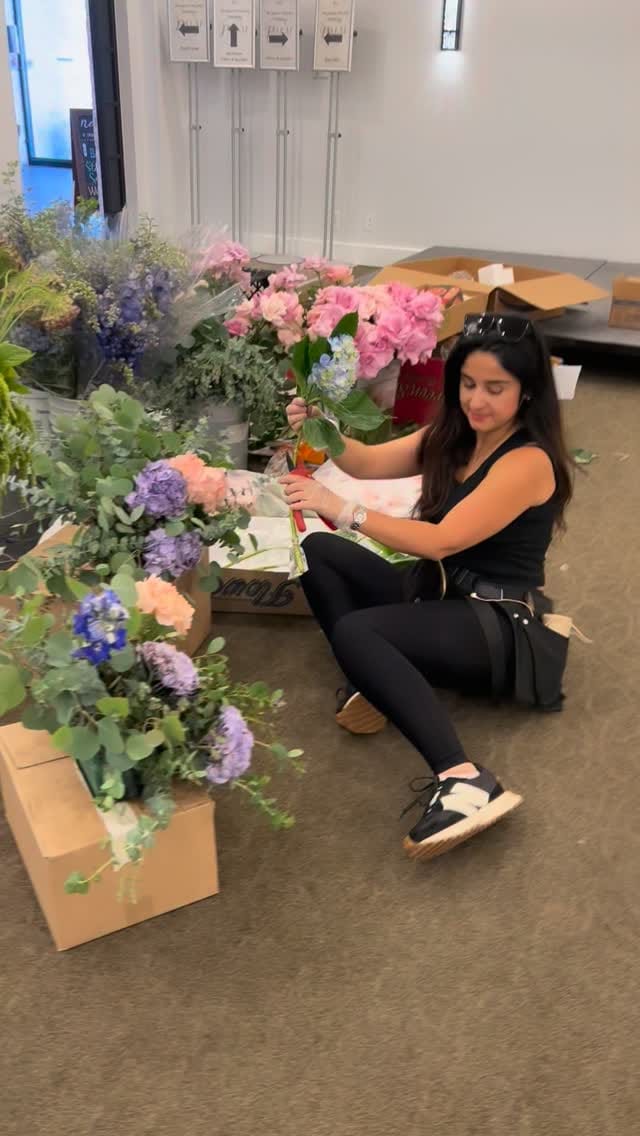 Bita sitting on the floor of an event space surrounded by flower boxes, holding pink hydrangea